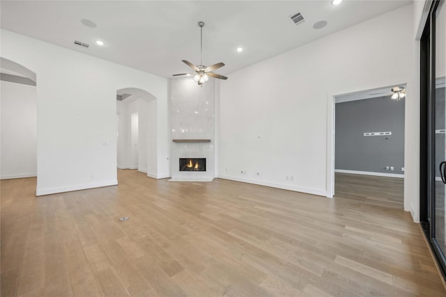 unfurnished living room featuring a fireplace, visible vents, arched walkways, and ceiling fan