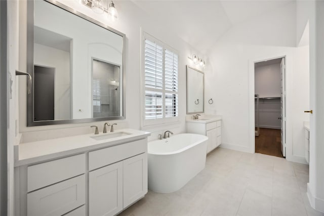 bathroom with two vanities, vaulted ceiling, a freestanding tub, and a sink