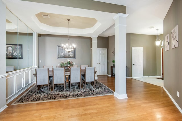 dining area featuring a tray ceiling, a notable chandelier, visible vents, light wood-type flooring, and ornate columns