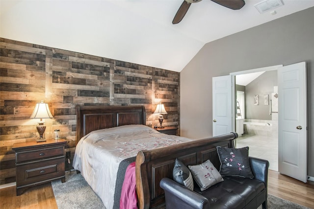 bedroom featuring wood walls, visible vents, vaulted ceiling, light wood finished floors, and ensuite bath