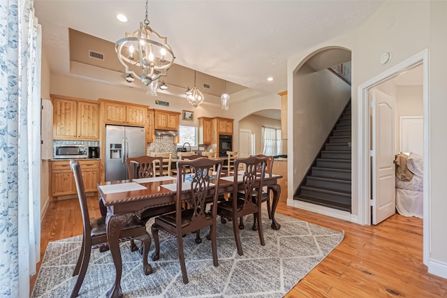 dining area featuring arched walkways, a tray ceiling, stairs, and light wood-style flooring