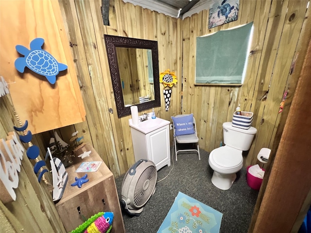 bathroom with toilet, wood walls, and vanity