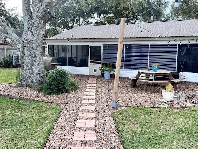 back of property with a lawn, a shingled roof, and a sunroom