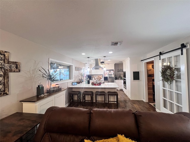 living area featuring visible vents, recessed lighting, dark wood-type flooring, and a barn door