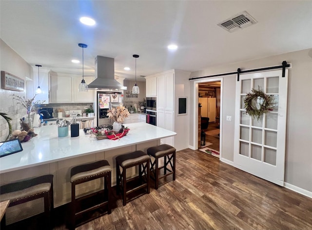 kitchen featuring visible vents, island exhaust hood, a barn door, stainless steel fridge, and a peninsula