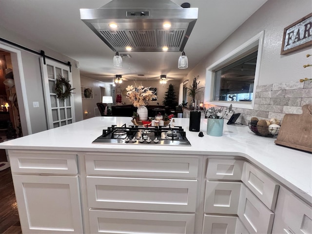 kitchen featuring range hood, white cabinetry, a barn door, light countertops, and stainless steel gas cooktop