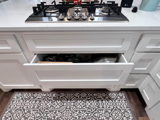 details with stainless steel gas cooktop, white cabinets, dark wood-type flooring, and light stone counters