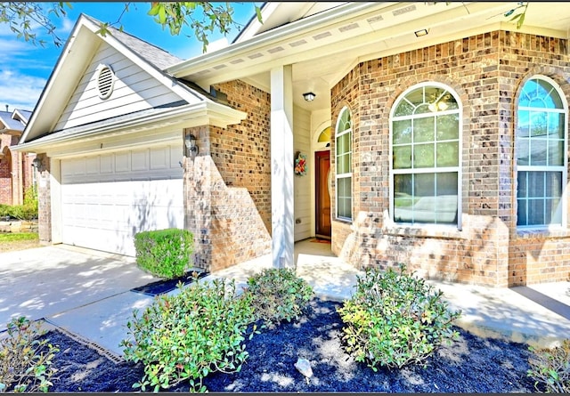 property entrance featuring an attached garage, driveway, and brick siding