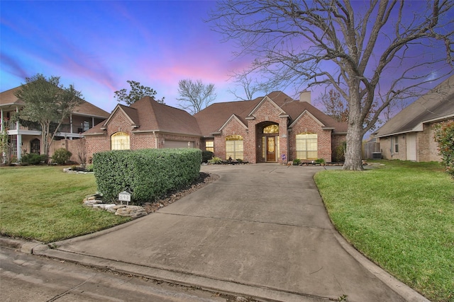 french provincial home featuring driveway, a chimney, a lawn, and brick siding