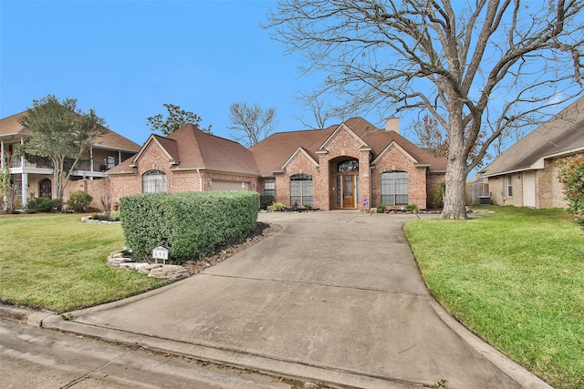 french country inspired facade featuring a front yard, concrete driveway, brick siding, and a chimney