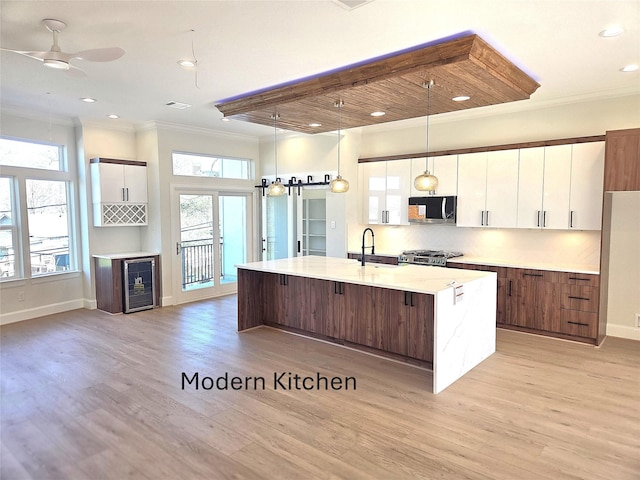 kitchen with beverage cooler, crown molding, white cabinetry, stainless steel microwave, and range