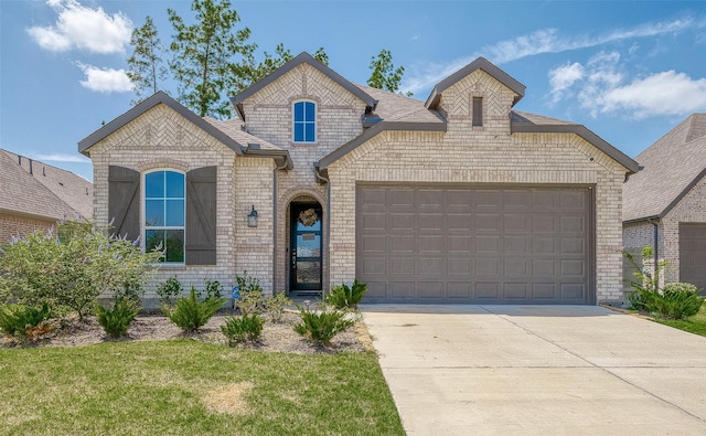 french country style house featuring an attached garage, brick siding, driveway, roof with shingles, and a front yard