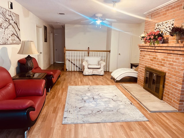 living area with ceiling fan, visible vents, a fireplace, and wood finished floors