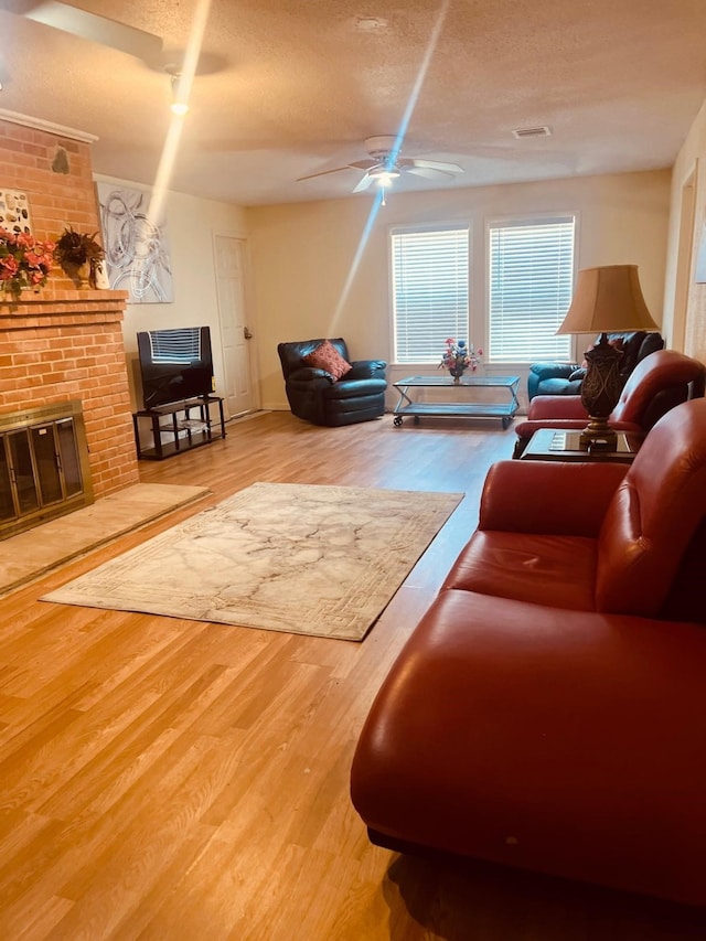 living room with a brick fireplace, visible vents, and wood finished floors