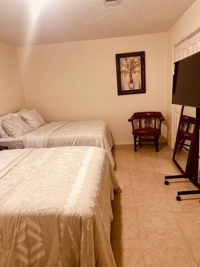 bedroom featuring light tile patterned floors, a textured ceiling, visible vents, and baseboards