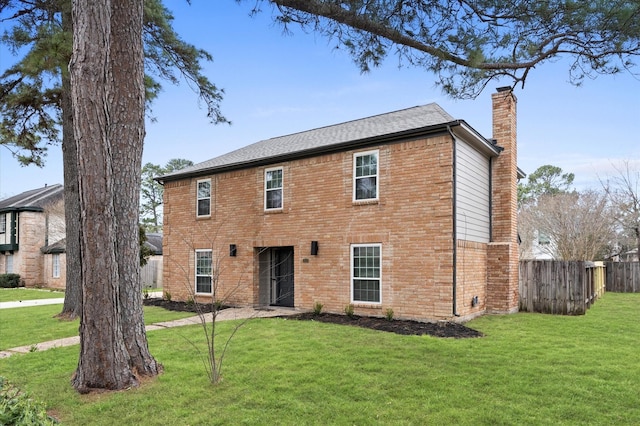 colonial home with a chimney, a front yard, fence, and brick siding