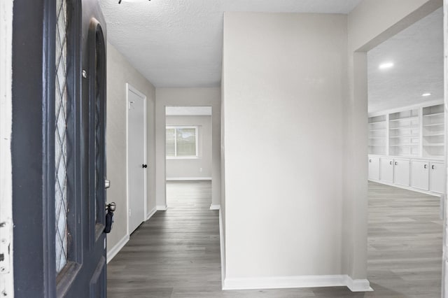 hall featuring a textured ceiling, built in shelves, dark wood-style floors, and baseboards