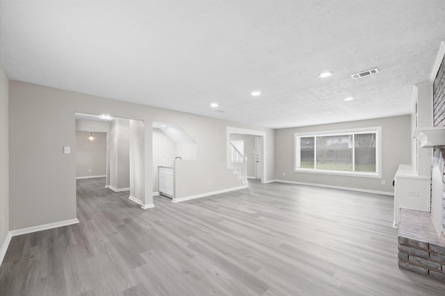 unfurnished living room with visible vents, light wood-style flooring, baseboards, and stairs