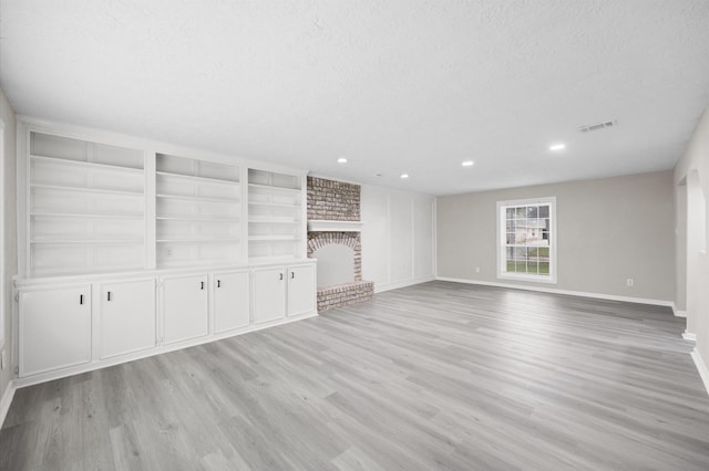 unfurnished living room featuring visible vents, baseboards, light wood-style flooring, a textured ceiling, and a brick fireplace