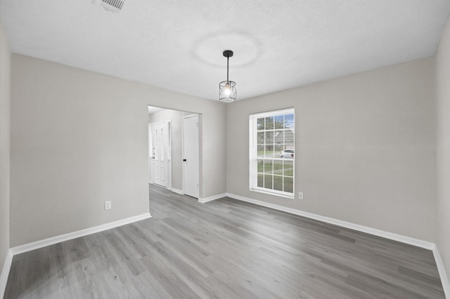 unfurnished room featuring a textured ceiling, wood finished floors, visible vents, and baseboards