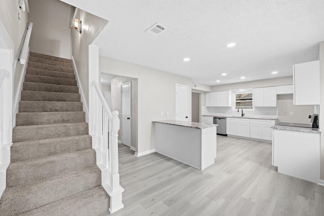 kitchen with visible vents, white cabinets, light stone countertops, stainless steel dishwasher, and a sink