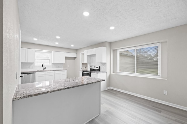 kitchen featuring baseboards, light stone counters, stainless steel appliances, light wood-style floors, and white cabinetry