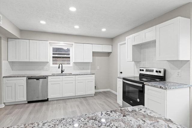 kitchen featuring stainless steel appliances, a sink, light wood-style floors, white cabinets, and light stone countertops