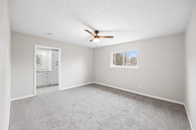 unfurnished bedroom with light carpet, baseboards, a textured ceiling, and ensuite bathroom