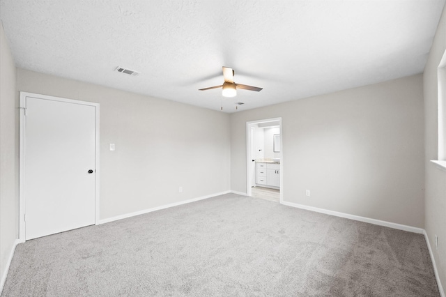 empty room with ceiling fan, a textured ceiling, light colored carpet, visible vents, and baseboards