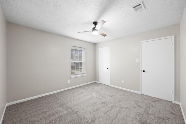 spare room featuring a textured ceiling, carpet floors, visible vents, baseboards, and a ceiling fan