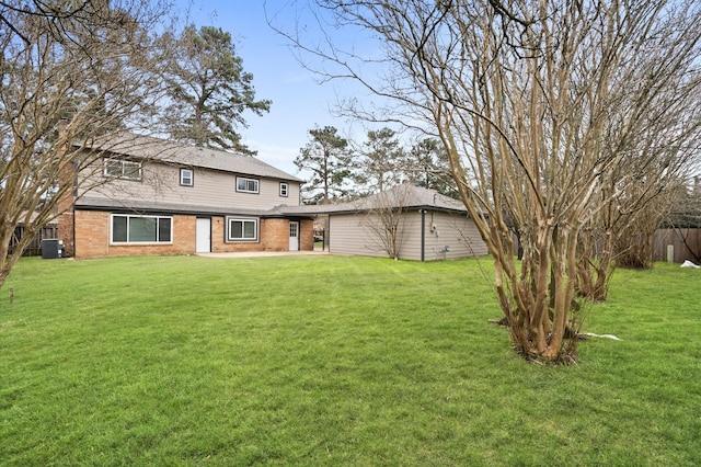 back of property with a yard, brick siding, central AC unit, and fence