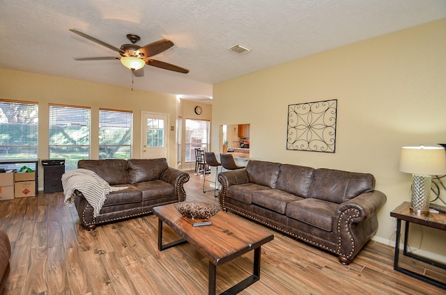 living area featuring a textured ceiling, wood finished floors, visible vents, baseboards, and a ceiling fan