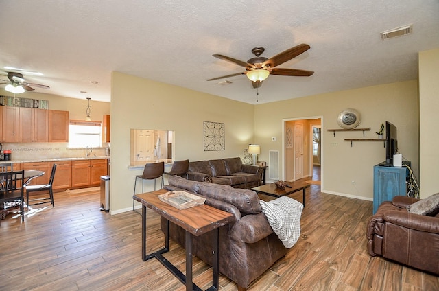 living area with ceiling fan, wood finished floors, visible vents, and baseboards