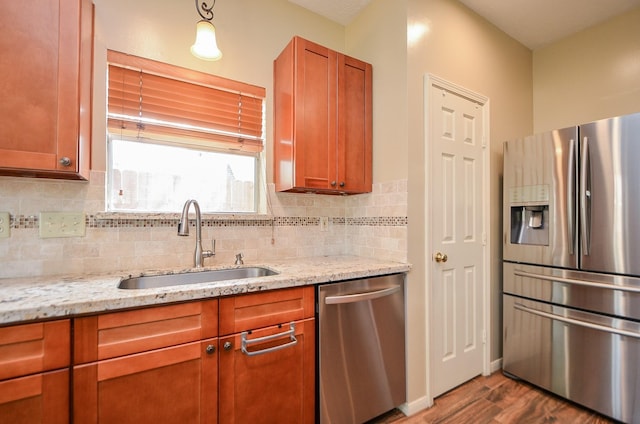 kitchen with stainless steel appliances, a sink, backsplash, light stone countertops, and dark wood-style floors