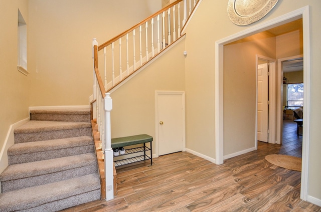 staircase featuring wood finished floors, a towering ceiling, and baseboards