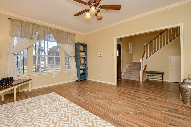 interior space with ornamental molding, a ceiling fan, wood finished floors, baseboards, and stairs