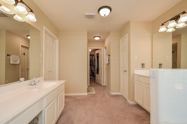 bathroom with vanity, visible vents, baseboards, carpet, and a walk in closet