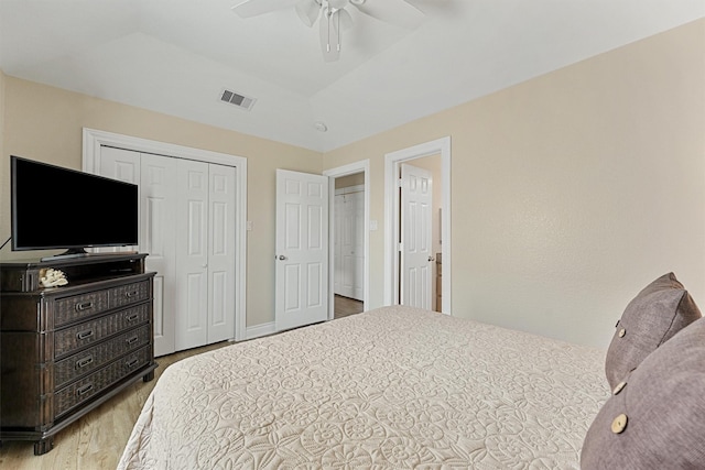 bedroom with a closet, visible vents, a raised ceiling, a ceiling fan, and wood finished floors