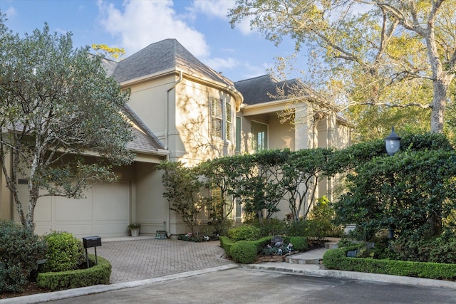 view of front of property featuring roof with shingles, decorative driveway, and stucco siding