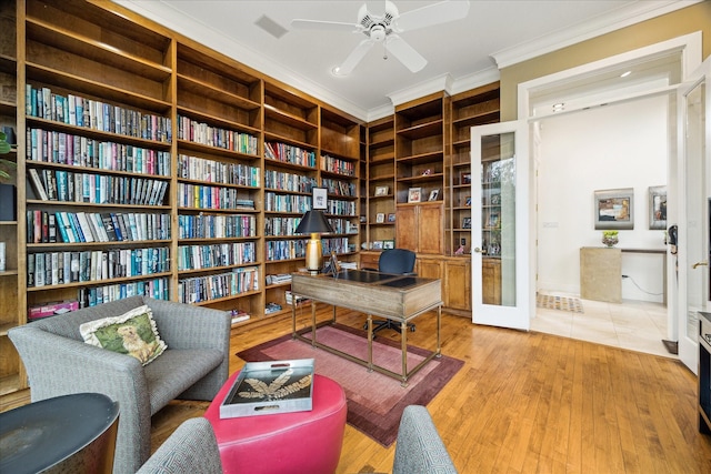 sitting room with ceiling fan, ornamental molding, french doors, wall of books, and light wood finished floors