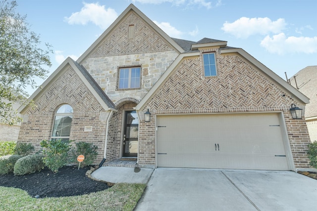 french country inspired facade featuring driveway, stone siding, an attached garage, and brick siding