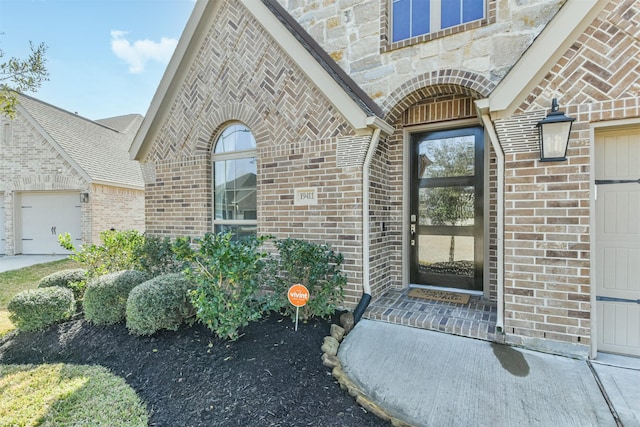 entrance to property with stone siding, brick siding, and an attached garage