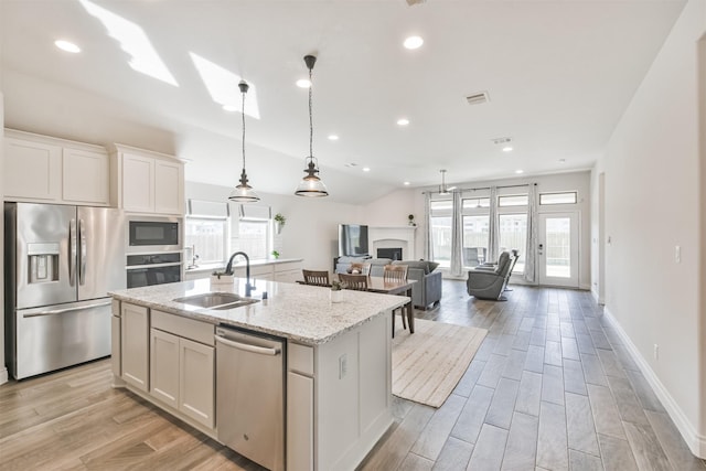 kitchen featuring light stone counters, a center island with sink, appliances with stainless steel finishes, white cabinets, and a sink