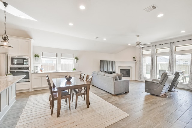 dining room with visible vents, a glass covered fireplace, lofted ceiling, light wood-style floors, and recessed lighting