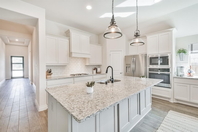 kitchen with a kitchen island with sink, a sink, white cabinetry, hanging light fixtures, and appliances with stainless steel finishes