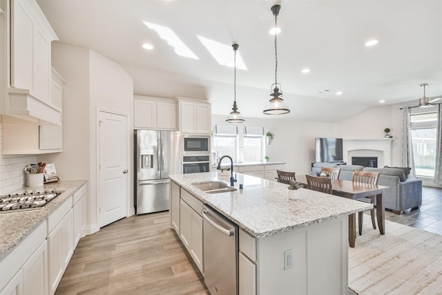 kitchen featuring white cabinets, decorative light fixtures, a kitchen island with sink, stainless steel appliances, and a sink