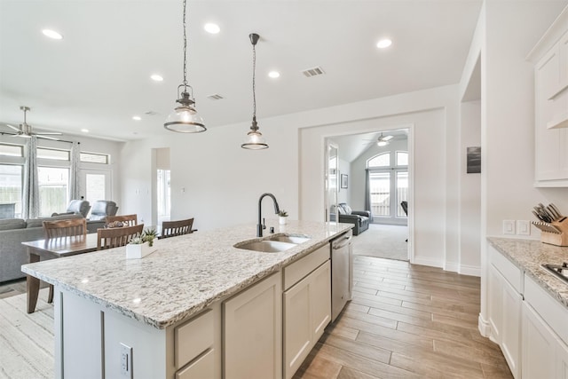 kitchen featuring dishwasher, open floor plan, light stone countertops, a kitchen island with sink, and a sink