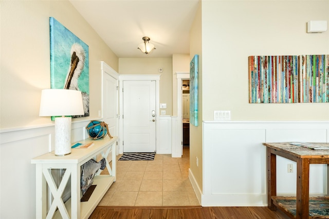 foyer entrance featuring a wainscoted wall, a decorative wall, and light tile patterned floors