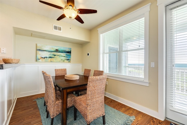 dining area with ceiling fan, a decorative wall, visible vents, baseboards, and dark wood-style floors