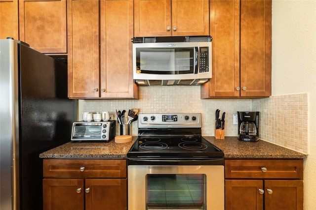 kitchen with a toaster, tasteful backsplash, dark stone counters, appliances with stainless steel finishes, and brown cabinets